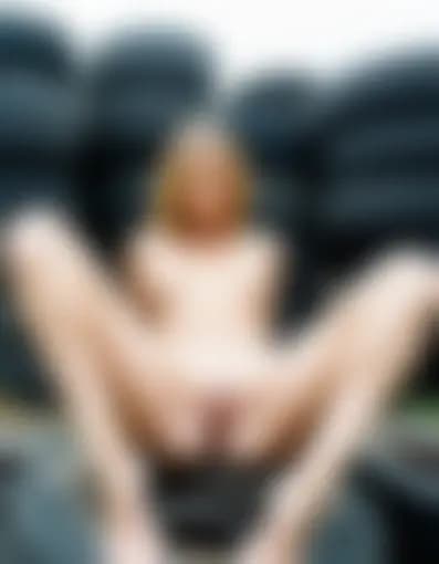 Natalie explores herself in an abandoned lot amongst rusted vehicles and tire stacks, fingering herself.