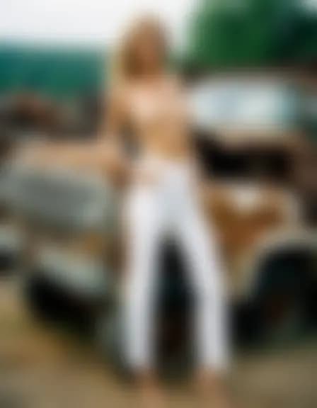 Natalie in a salvage lot, amidst rusted cars. Focused on a sensual act, with car hulks towering around them, adding a gritty backdrop.