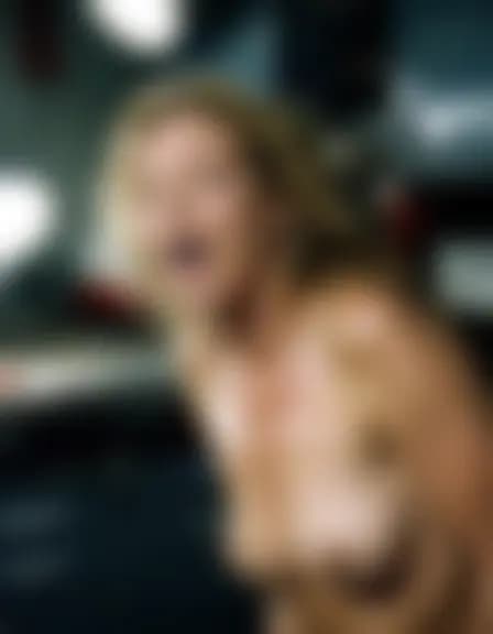 Natalie experiencing orgasm in a dimly lit auto repair shop, illuminated by emergency lights near a workbench.
